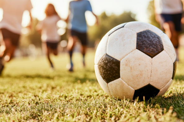 close up of soccer ball on grass with players running in background, capturing excitement of game A close up of soccer ball on grass with players running in background, capturing excitement of game